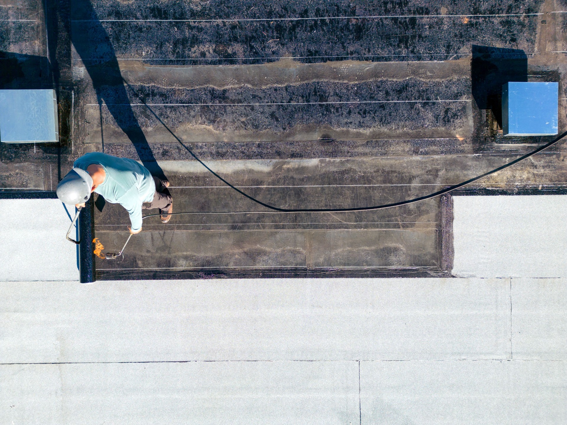 Roofer applying torch to bitumen membrane on torch down roof