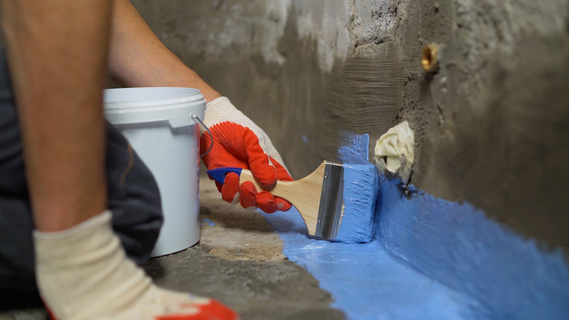 Waterproofing the floor with a brush.Waterproofing concrete mortar. The master puts waterproofing on a concrete floor with a brush. Bathroom floor waterproofing.