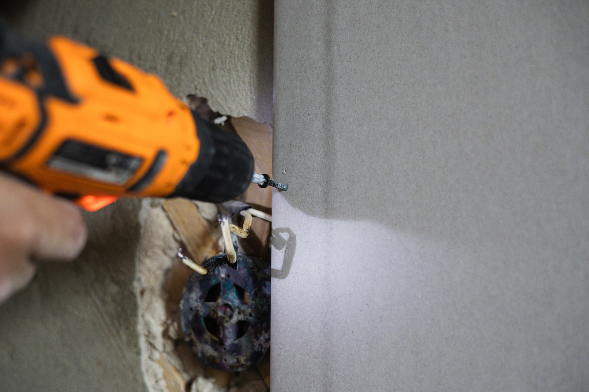 Close-up of a builder using a drill to install drywall during a home renovation, demonstrating the process of attaching building materials. Attaching a sheet of drywall to a wall using screws.