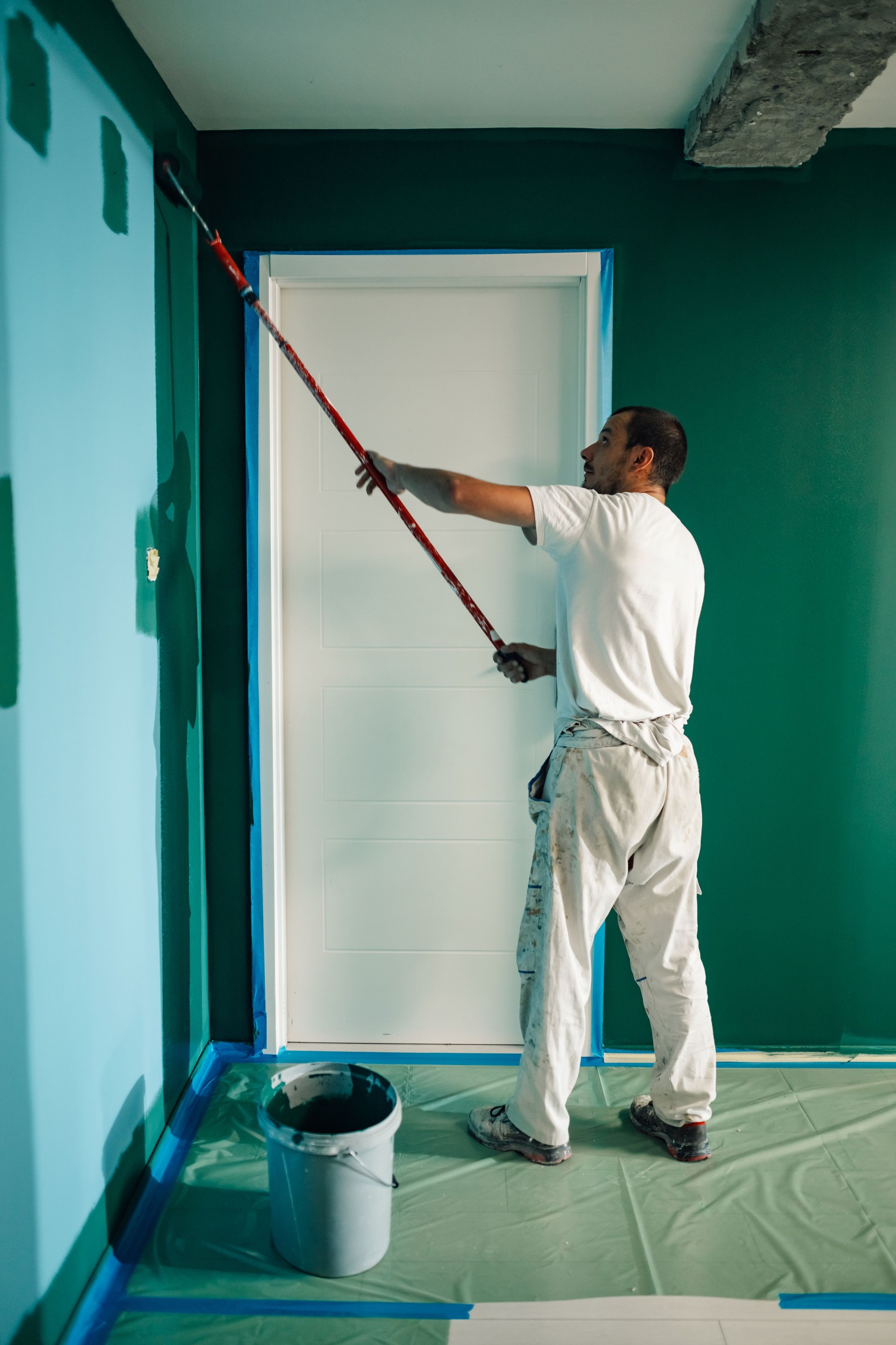 Painter using a roller applying green paint on wall